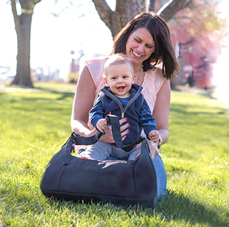 A smiling mother holds her toddler at the park, a Medela Breast Pump Bag in one hand and easily transportable.